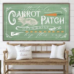 May include: A green sign with white lettering that reads "Cottontails' Carrot Patch Open Daily Hop This Way". A white rabbit illustration is on the sign with a carrot above it. The sign is hanging on a white shiplap wall above a wooden bench with white pillows.