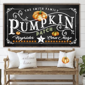 May include: A black chalkboard sign with white lettering that reads "The Smith Family Pumpkin Patch Hayrides 5&cent; Corn Maze". The sign is decorated with orange pumpkins and stars.