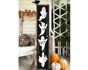 May include: Black and white wooden sign with a spooky Halloween theme. The sign features five ghosts with spiderwebs and the word "BOO" on one of the ghosts. The sign is hanging on a white wooden door with a wreath and a broom.
