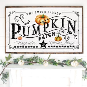 May include: A white wooden sign with black text that reads "The Smith Family Pumpkin Patch Hayrides 5&cent; Corn Maze". The sign has a brown wooden frame and features a stylized pumpkin design with orange and green accents.