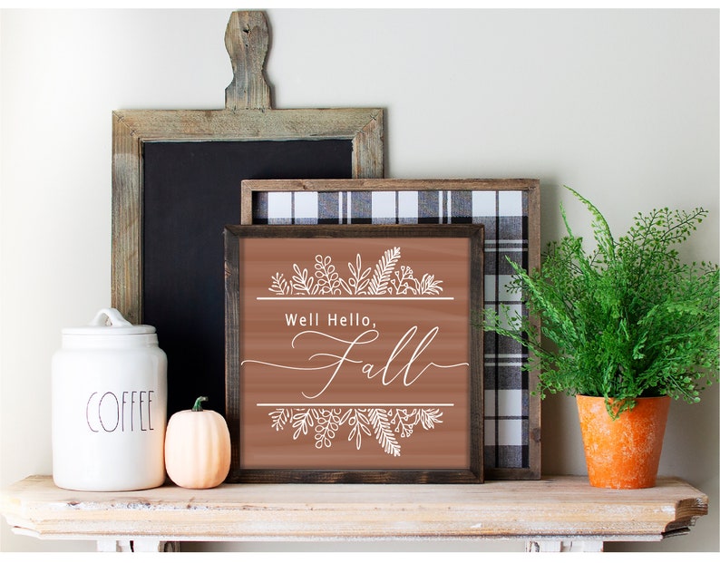 May include: A brown wooden sign with the text "Well Hello, Fall" in white script. The sign is decorated with white floral designs and has a rustic wood frame.