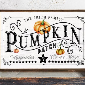 May include: A white wooden sign with black text that reads "The Smith Family Pumpkin Patch Hayrides $5 Corn Maze". The sign has a brown wooden frame and is decorated with fall-themed illustrations, including pumpkins and vines.