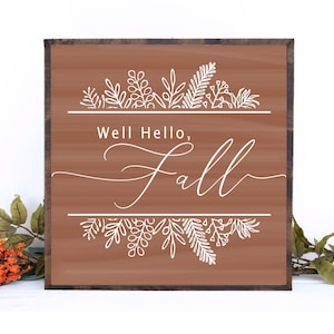 May include: A brown wooden sign with the text "Well Hello, Fall" in white cursive lettering. The sign is decorated with white floral designs at the top and bottom.