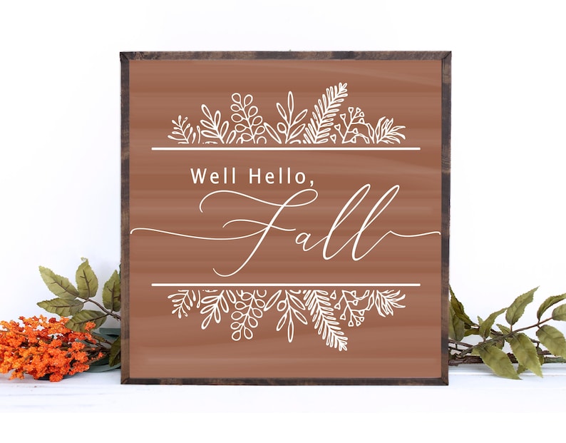 May include: A brown wooden sign with the text "Well Hello, Fall" in white cursive lettering. The sign is decorated with white floral designs at the top and bottom.