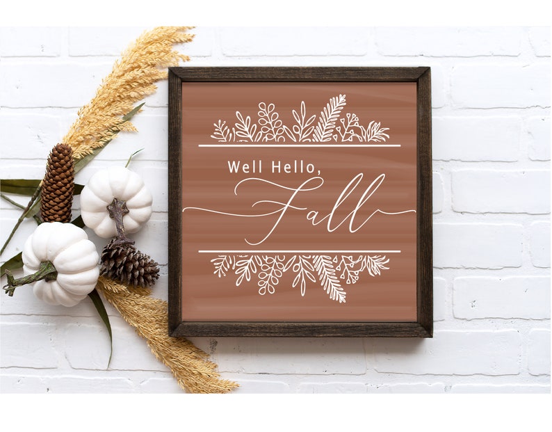 May include: A brown wooden framed sign with the text "Well Hello, Fall" in white cursive font. The sign is decorated with white floral designs at the top and bottom.