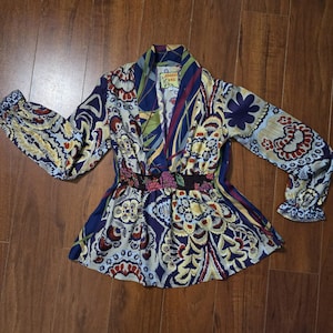 Pode incluir: Uma blusa de manga comprida com um padr&atilde;o floral e paisley multicolorido vibrante em tons de azul marinho, creme, vermelho e verde. A pe&ccedil;a apresenta um decote em V profundo, uma cintura el&aacute;stica franzida e punhos com folhos com uma etiqueta Johnny Was.
