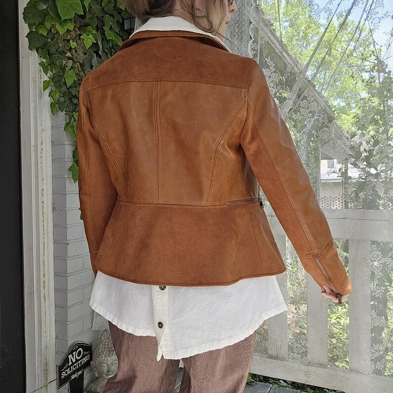 May include: A brown leather jacket with a white collar and a peplum waist. The jacket has a zipper on the sleeve and a button-down white shirt underneath. The person is wearing brown corduroy pants.