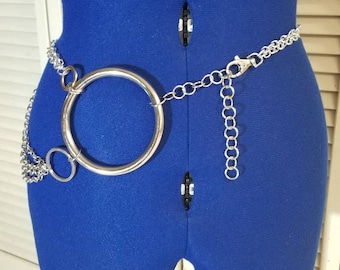 Puede incluir: Un cinturón de cadena plateado con un anillo grande, redondo y plateado. El cinturón está en un maniquí de vestido azul.