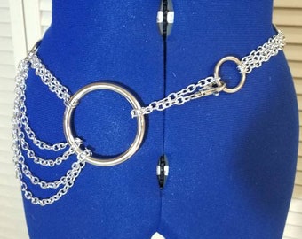 Puede incluir: Cadena de cuerpo plateada con una pieza central circular grande y múltiples cadenas colgantes. La cadena está colocada sobre un maniquí azul, mostrando su diseño. Esta joya es un accesorio de moda.