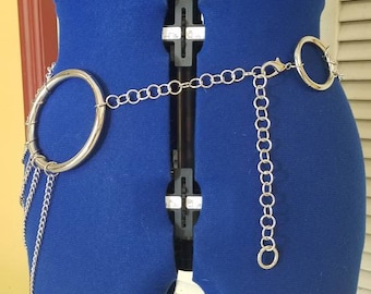 Puede incluir: Un cinturón de cadena plateado con un gran anillo circular y una cadena colgante. El cinturón está en un maniquí de tela azul.