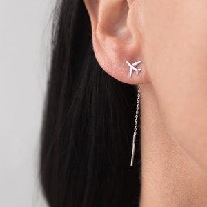 May include: Silver airplane dangle earrings with a small airplane charm at the top and a long chain with a small silver bar at the bottom.