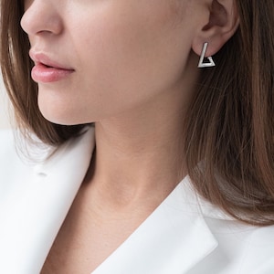 Op de afbeelding: Een paar zilveren driehoekige oorbellen. De oorbellen zijn simpel en modern, met een strak, geometrisch ontwerp.