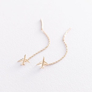 May include: A pair of gold airplane dangle earrings with a delicate chain. The earrings are a simple and stylish design.