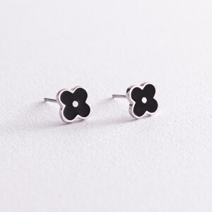 Könnte beinhalten: Ein Paar silberne Ohrstecker mit schwarzen, blumenförmigen Akzenten. Jeder Ohrstecker hat eine vierblättrige Blume mit einem kleinen Kreis in der Mitte.
