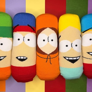 May include: Five pairs of character socks, each featuring a different design from a popular animated series. The socks have a tan base with colorful accents, including green, blue, red, orange, and yellow. Each pair has a smiling face.