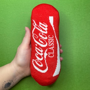 May include: Red and white Coca-Cola sock with the words "Coca-Cola Classic" printed on it.