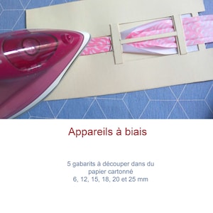 Può includere: Un nastro di sbieco rosa e bianco viene stirato con un ferro da stiro rosa su un modello di cartone bianco. Il modello ha cinque fessure ritagliate per diverse dimensioni di nastro di sbieco: 6, 12, 15, 18, 20 e 25 mm. Il testo "Appareils à biais" è scritto in rosso sotto il modello. Il testo "5 gabarits à découper dans du papier cartonné 6, 12, 15, 18, 20 et 25 mm" è scritto sotto il testo "Appareils à biais". Il testo "Petit Citron la couture pour tous" è scritto in nero sotto il testo.