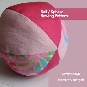Op de afbeelding: Een handgemaakte stoffen bal met een patchwork-ontwerp. De bal heeft segmenten van roze, lichtroze en stof met bloemenpatroon. De tekst op de afbeelding luidt "Ball / Sphere Sewing Pattern" en "Sew your own In French & in English".