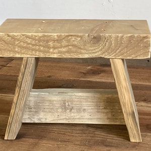 May include: A small, rustic wooden stool with a rectangular top and angled legs. The wood has a natural, weathered appearance, showcasing the grain and knots. The stool is approximately 30 cm long, 20 cm wide, and 25 cm tall.