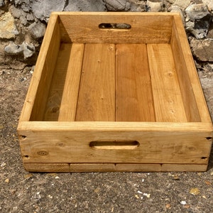 May include: A rectangular wooden tray with two handles on the sides and one on the front. The tray is made of natural wood and has a light brown stain.