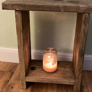 May include: A rustic wooden side table with a single shelf and a lit candle in a glass jar on the shelf.
