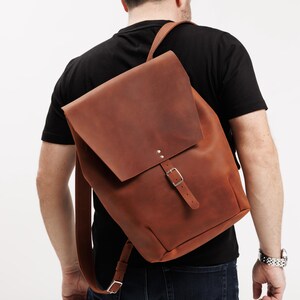 May include: A brown leather backpack with a flap closure and adjustable straps. The backpack features a buckle closure and is worn over the shoulders. The bag is approximately 16 inches tall and 12 inches wide.