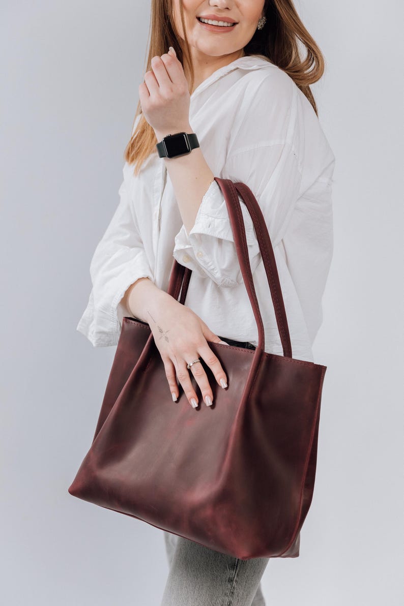 May include: A burgundy leather tote bag with two handles. The bag is large enough to carry everyday essentials.