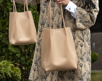 Könnte beinhalten: Zwei beigefarbene Ledertaschen mit einem Blumenmuster im Hintergrund. Die größere Tasche hat ein weißes Etikett mit dem Text "Weekend Bag" darauf.
