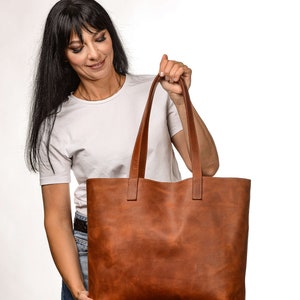 Op de afbeelding: Een bruine leren tote bag met twee handvatten. De tas is groot en ruim, en perfect voor het dragen van dagelijkse benodigdheden.