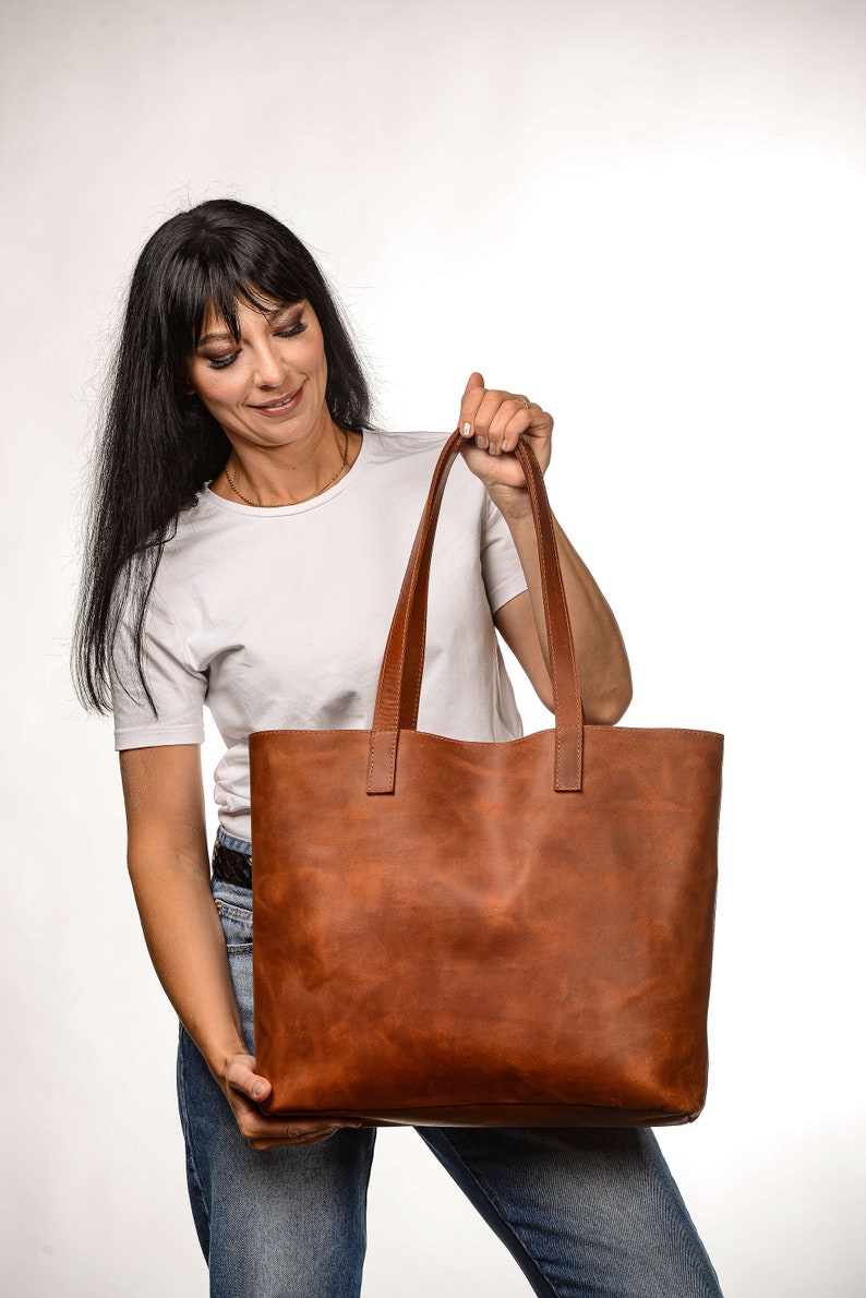 Op de afbeelding: Een bruine leren tote bag met twee handvatten. De tas is groot en ruim, en perfect voor het dragen van dagelijkse benodigdheden.