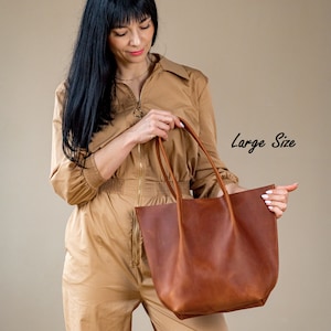 May include: A brown leather tote bag with a large size label. The bag has a wide opening and two handles.