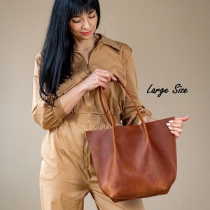 Pu&ograve; includere: Una borsa tote in pelle marrone con un'etichetta 'Taglia Grande'. La borsa ha un'ampia apertura e due manici.