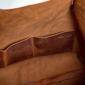 May include: The inside of a brown leather tote bag with two interior pockets. The bag has a leather label that reads "Custom Made in the USA".