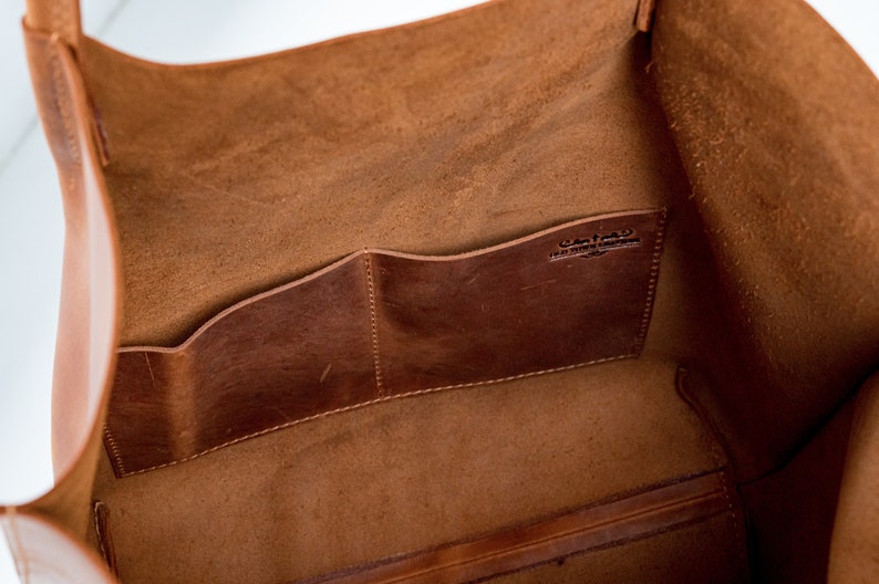 May include: The inside of a brown leather tote bag with two interior pockets. The bag has a leather label that reads "Custom Made in the USA".