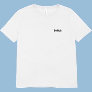 Puede incluir: Una camiseta blanca con la palabra "Switch" impresa en negro en la parte delantera. La camiseta tiene mangas cortas y cuello redondo. El fondo es azul claro.