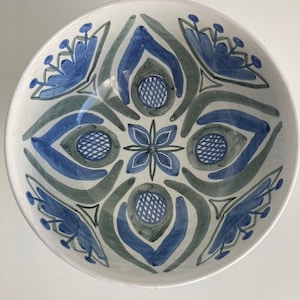 Puede incluir: Un tazón de cerámica blanco con un patrón geométrico azul y verde. El patrón presenta flores estilizadas y círculos.