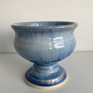 Op de afbeelding: Een blauwe en witte keramische voetkom met een geglazuurde afwerking. De kom heeft een brede, ronde basis en een hoge, slanke steel.