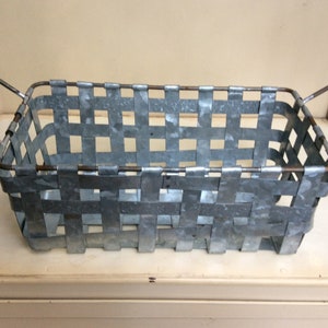 May include: A rectangular metal basket with two handles. The basket is made of woven metal strips and has a galvanized finish.