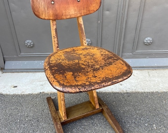 May include: A vintage wooden chair with a worn brown leather seat and a simple design. The chair has a unique angled back and a sturdy base.