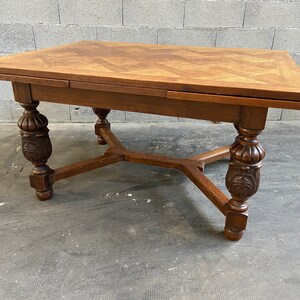 Könnte beinhalten: Ein dunkelbrauner Holztisch mit einem Parkett-Oberteil und geschnitzten Beinen. Der Tisch hat auf jeder Seite eine Klappplatte.
