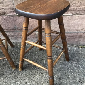 Op de afbeelding: Twee houten barkrukken met een donkerbruine afwerking. De krukken hebben een ronde zitting en een eenvoudig, stevig ontwerp.