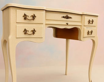 May include: Cream-colored vanity desk with curved legs and ornate brass drawer pulls. The desk has multiple drawers and a central opening for a chair. The design is vintage and elegant, suitable for a bedroom or dressing area.