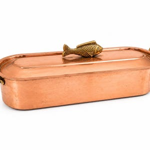 Peut inclure: Un plat à rôtir rectangulaire en cuivre avec un couvercle et des poignées en laiton. Le couvercle est surmonté d'une poignée en forme de poisson en laiton. Le plat est en cuivre et a une finition polie.