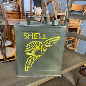 Puede incluir: Un bidón de gasolina de metal verde con un logotipo de Shell amarillo y un diseño de concha marina alada. El bidón tiene una tapa negra y un asa.