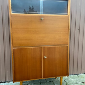 Può includere: Una scrivania vintage in legno con un armadio superiore in vetro e due ante inferiori. La scrivania ha una finitura in legno chiaro e ferramenta in ottone.