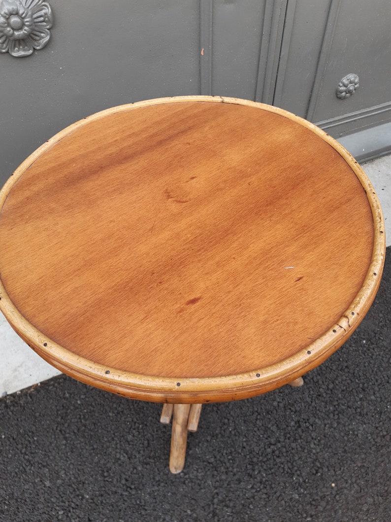 Puede incluir: Una mesa redonda de madera con un acabado de madera natural y un borde de bamb&uacute; tejido. La mesa tiene una base de tr&iacute;pode hecha de bamb&uacute; tejido.
