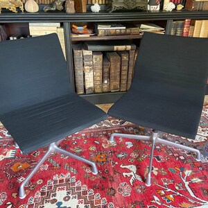 Peut inclure: Deux chaises de bureau noires avec des pieds en métal argenté sur un tapis rouge à motifs.