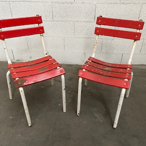May include: Two red metal chairs with white painted frames. The chairs have a slatted seat and back.