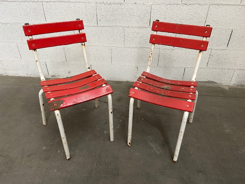 May include: Two red metal chairs with white painted frames. The chairs have a slatted seat and back.