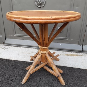 May include: A round, wooden table with a woven top and a unique, tripod-style base. The table is made of natural, light brown wood and has a rustic, vintage look.